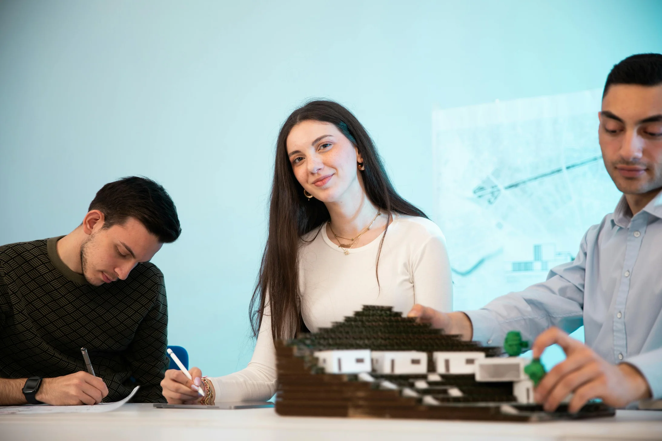 Three people collaborating on an architectural model in an office setting, emphasizing teamwork.