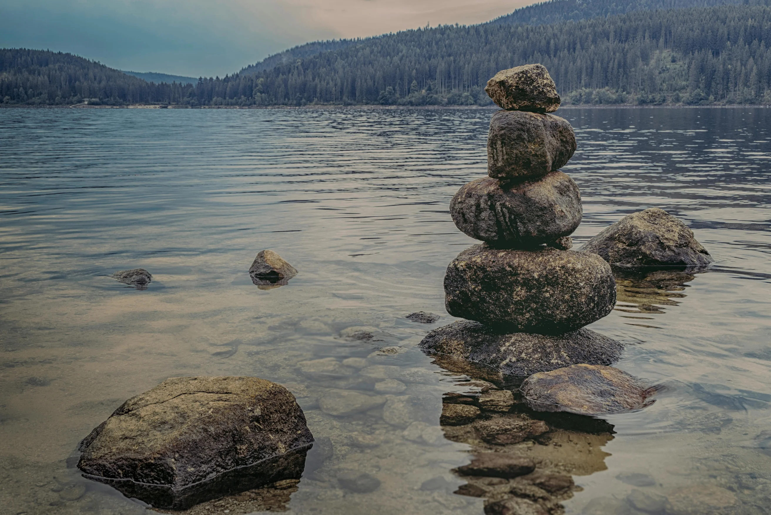Peaceful lake scene at Schluchsee, Germany, showcasing rock balancing and scenic nature.