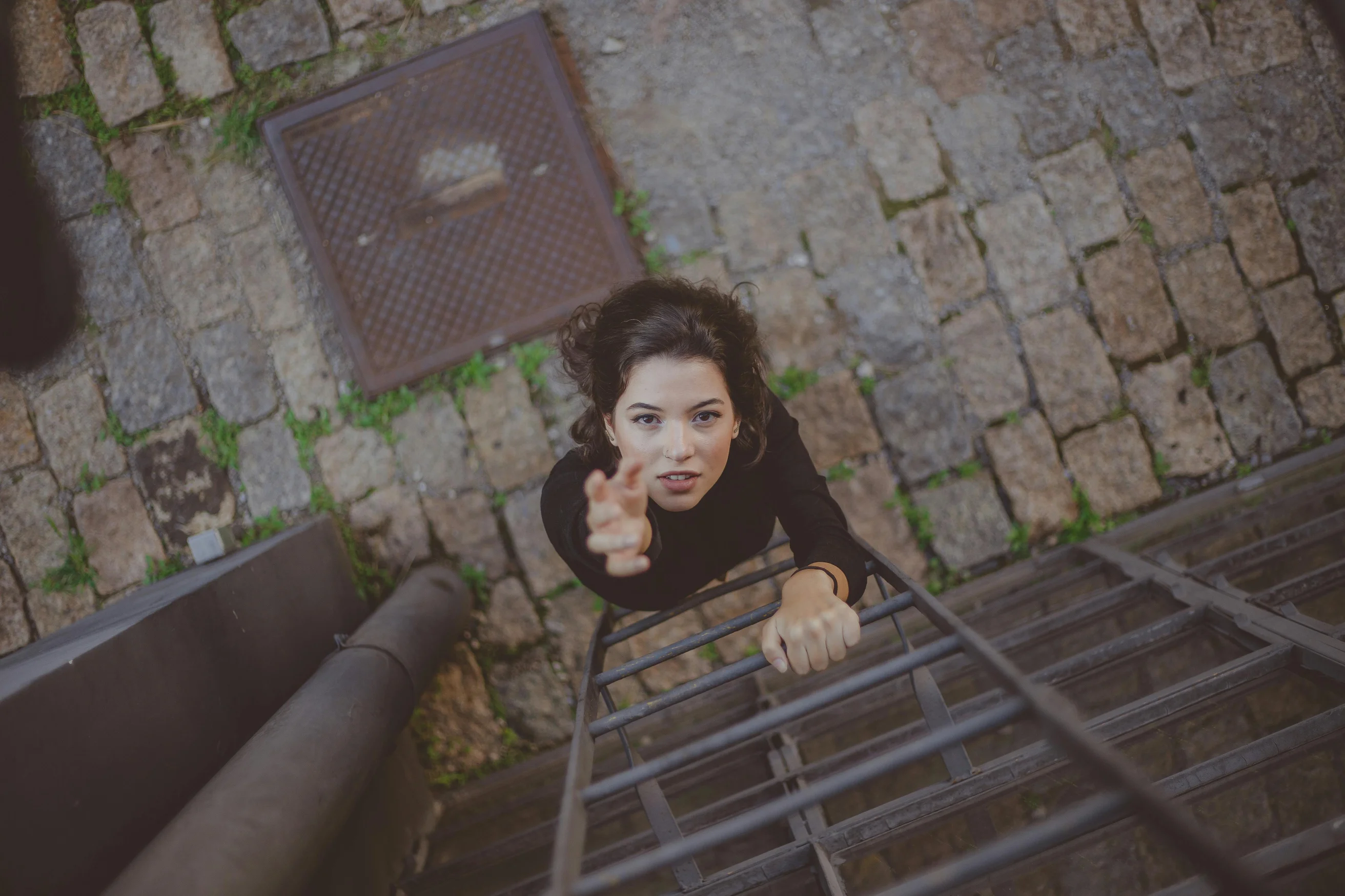 A woman reaching upwards while climbing a ladder on a stone pathway, captured from above.
