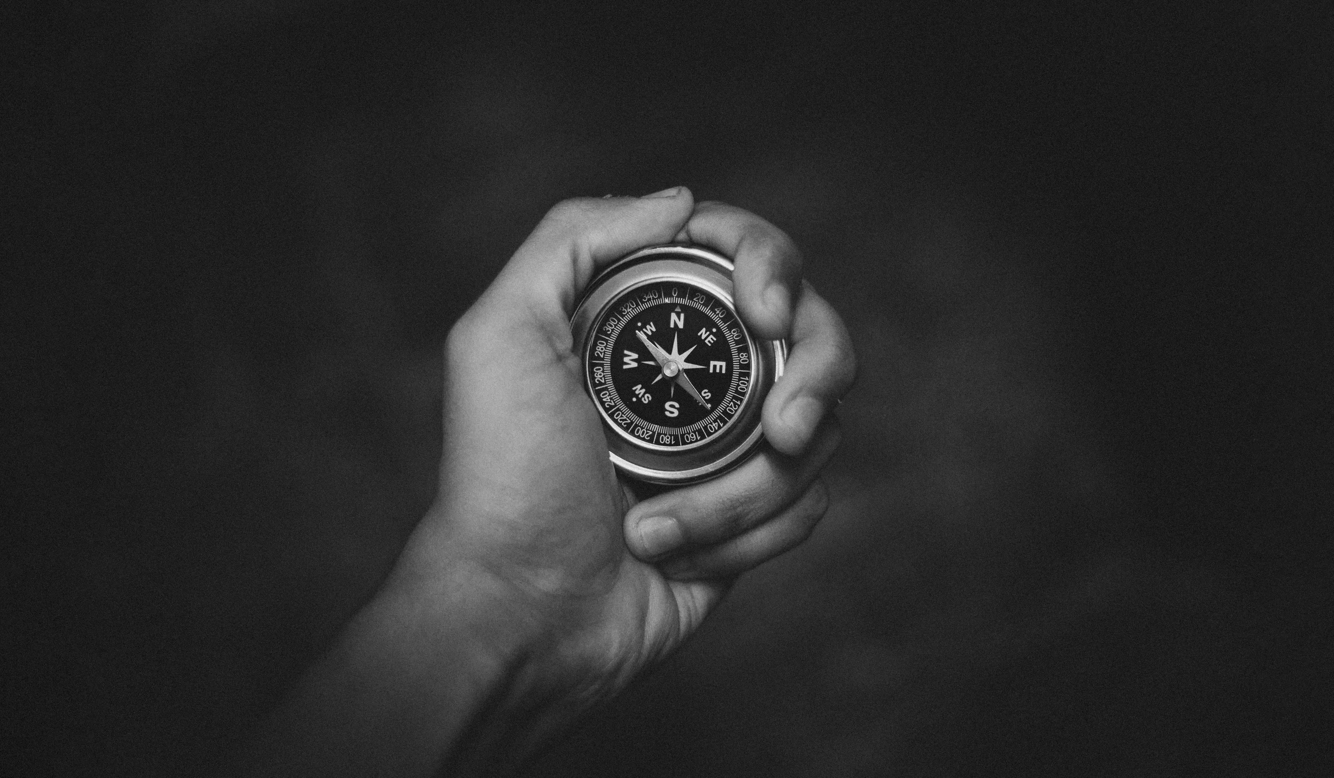 A black and white close-up of a hand holding a compass, symbolizing exploration.
