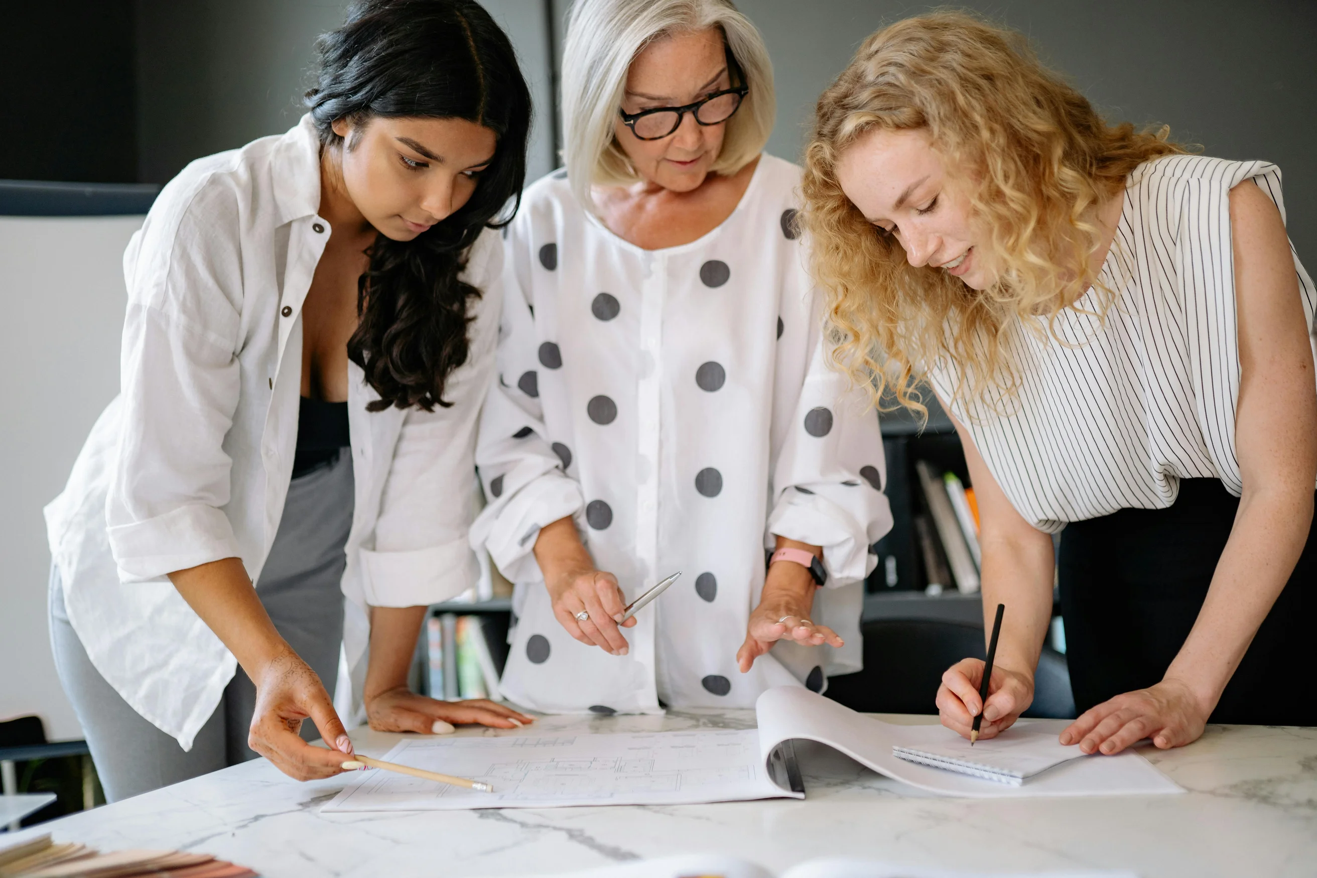 Three women working together over documents on a marble table indoors, showcasing teamwork and planning.