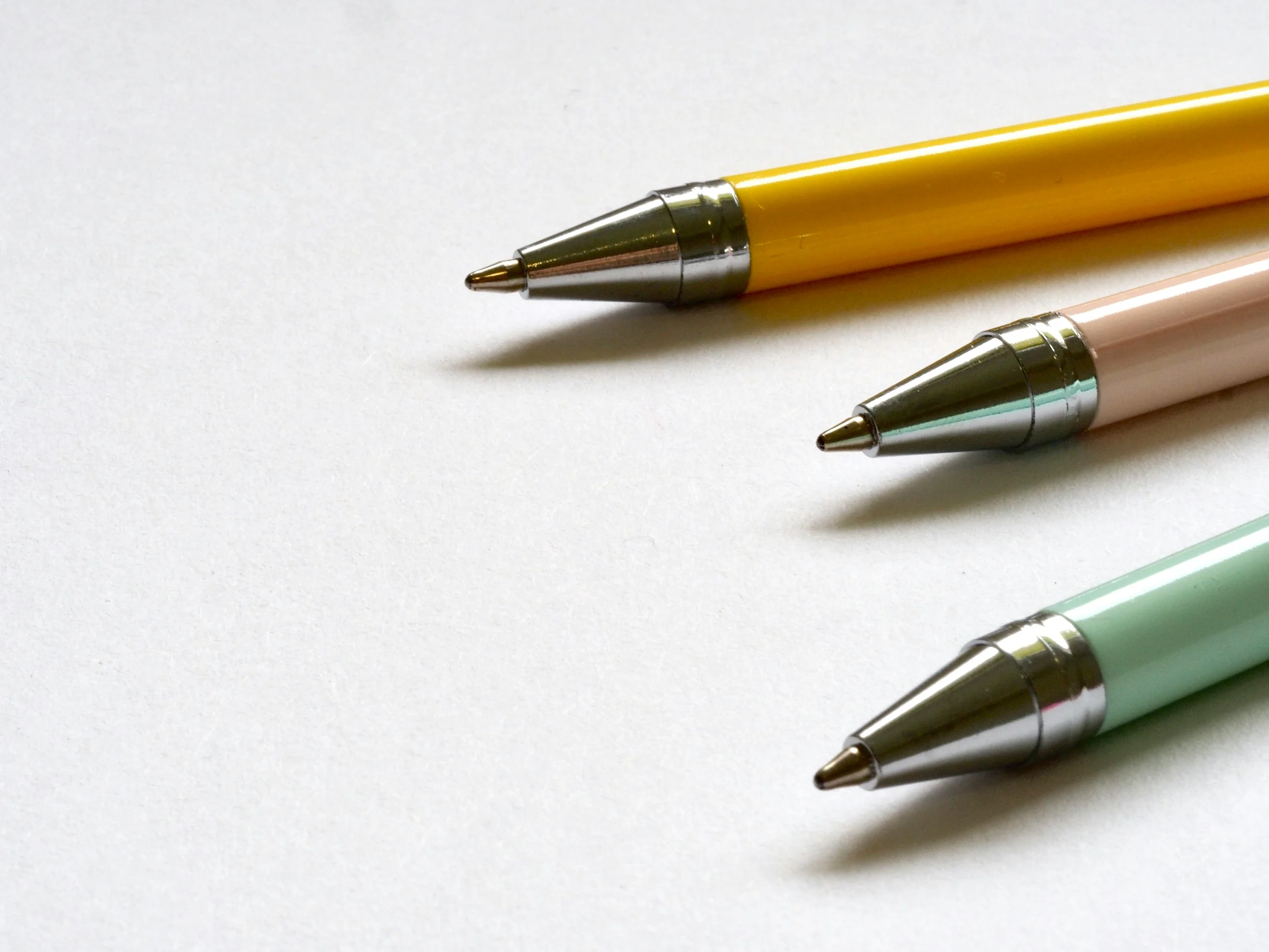 Three multicolored ballpoint pens lay on a clean white surface in a minimal style.