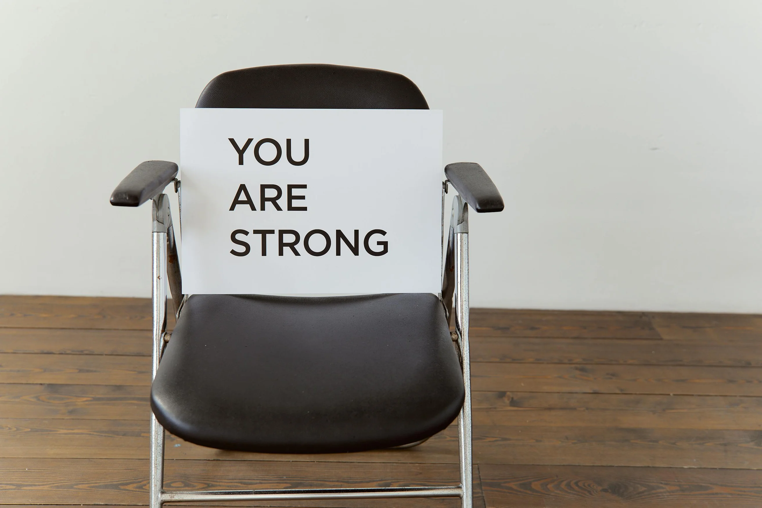 Black chair with 'You Are Strong' sign, symbolizing resilience.