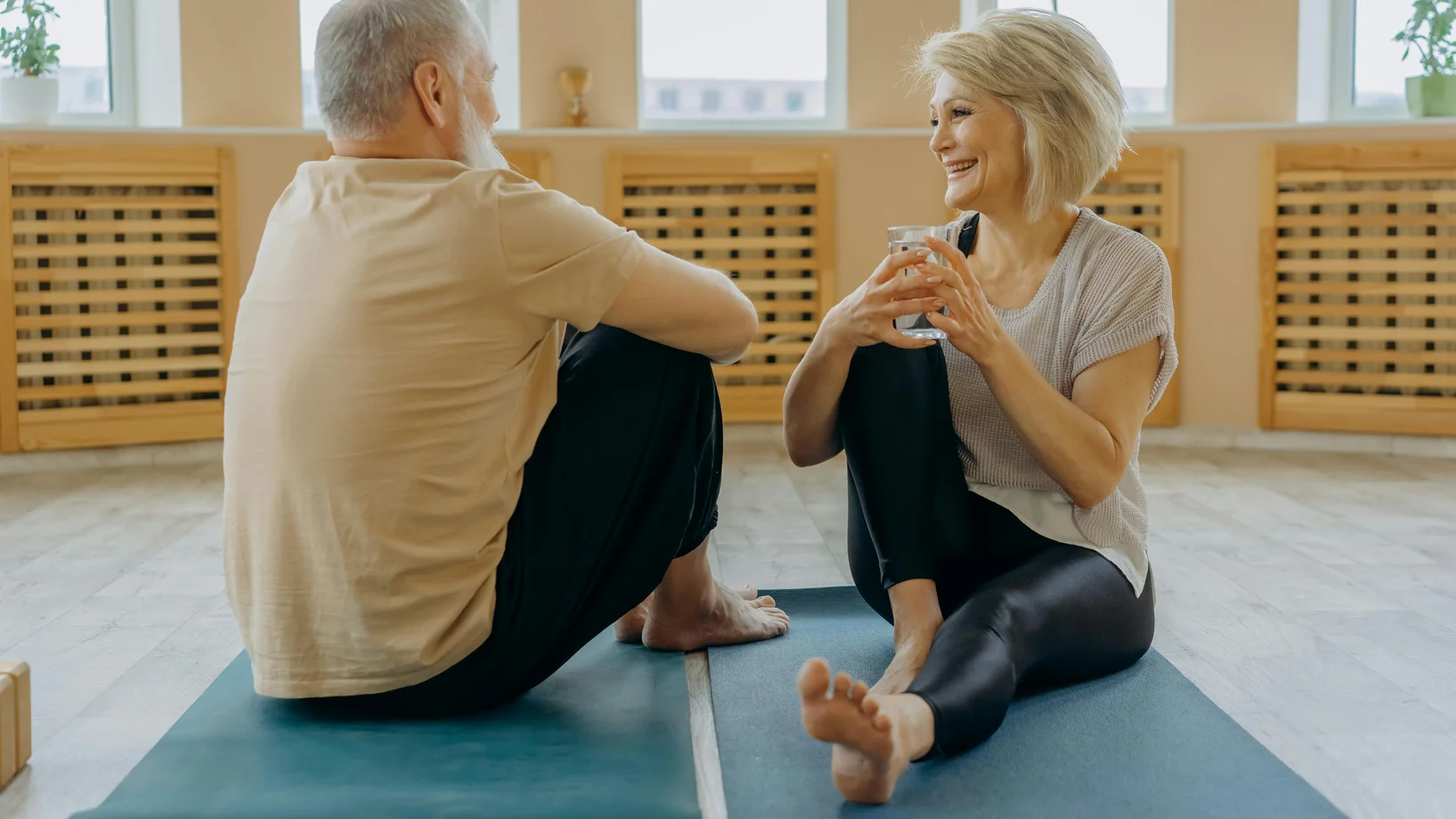 An elderly man and woman having conversation while sitting on yoga mats