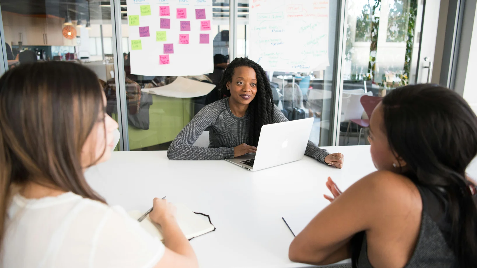 A diverse group of women collaborates around a desk in a modern office setting.