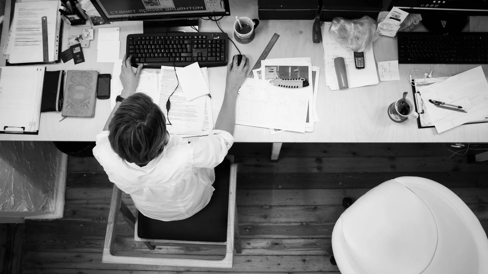 Black and white image of an employee working at a desk with papers and computer.