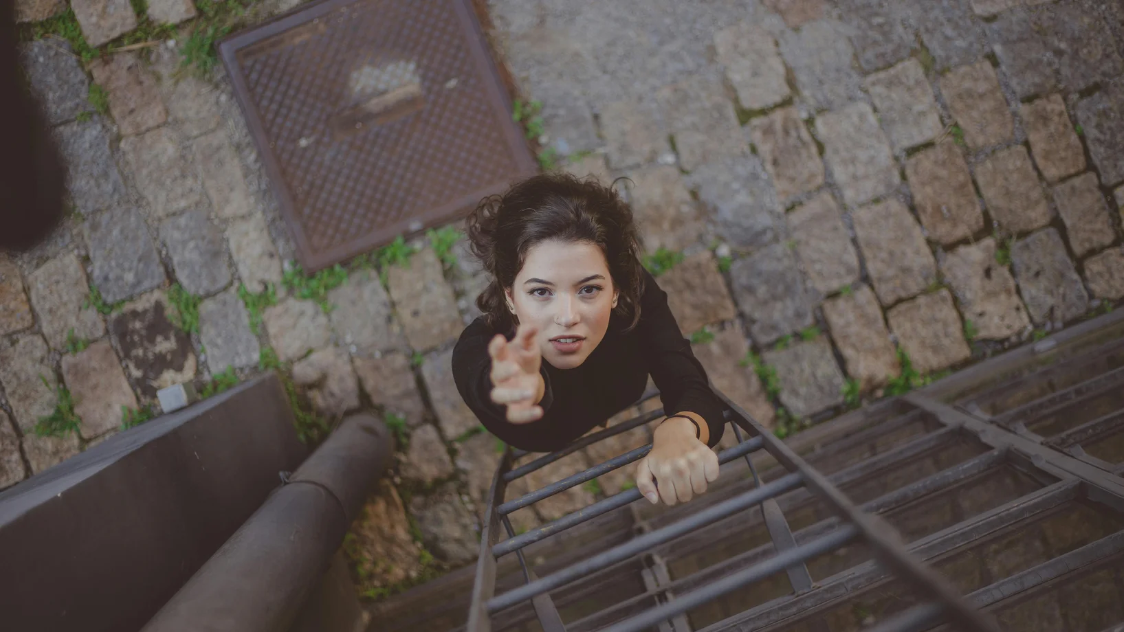 A woman reaching upwards while climbing a ladder on a stone pathway, captured from above.