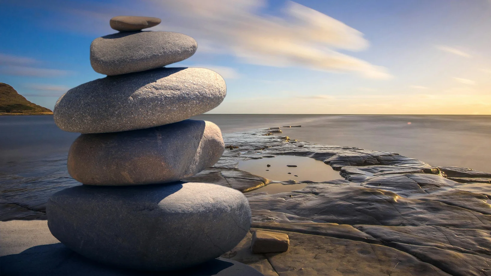 A serene stack of stones on the rocky seashore during a peaceful sunrise, embodying balance and zen.