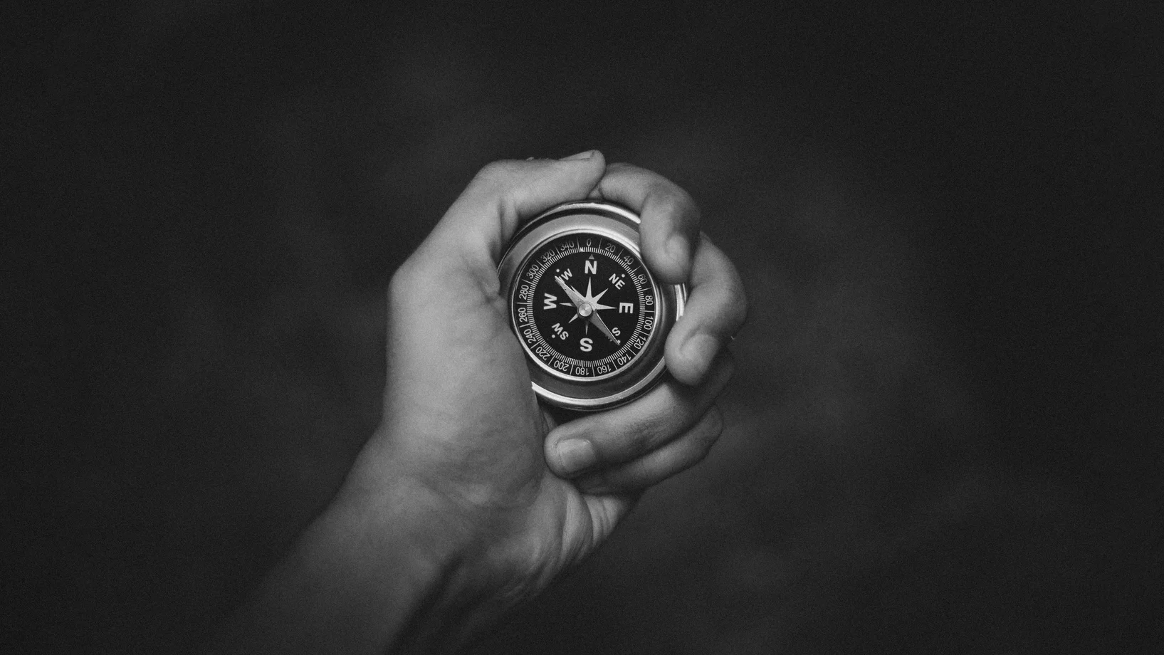 A black and white close-up of a hand holding a compass, symbolizing exploration.