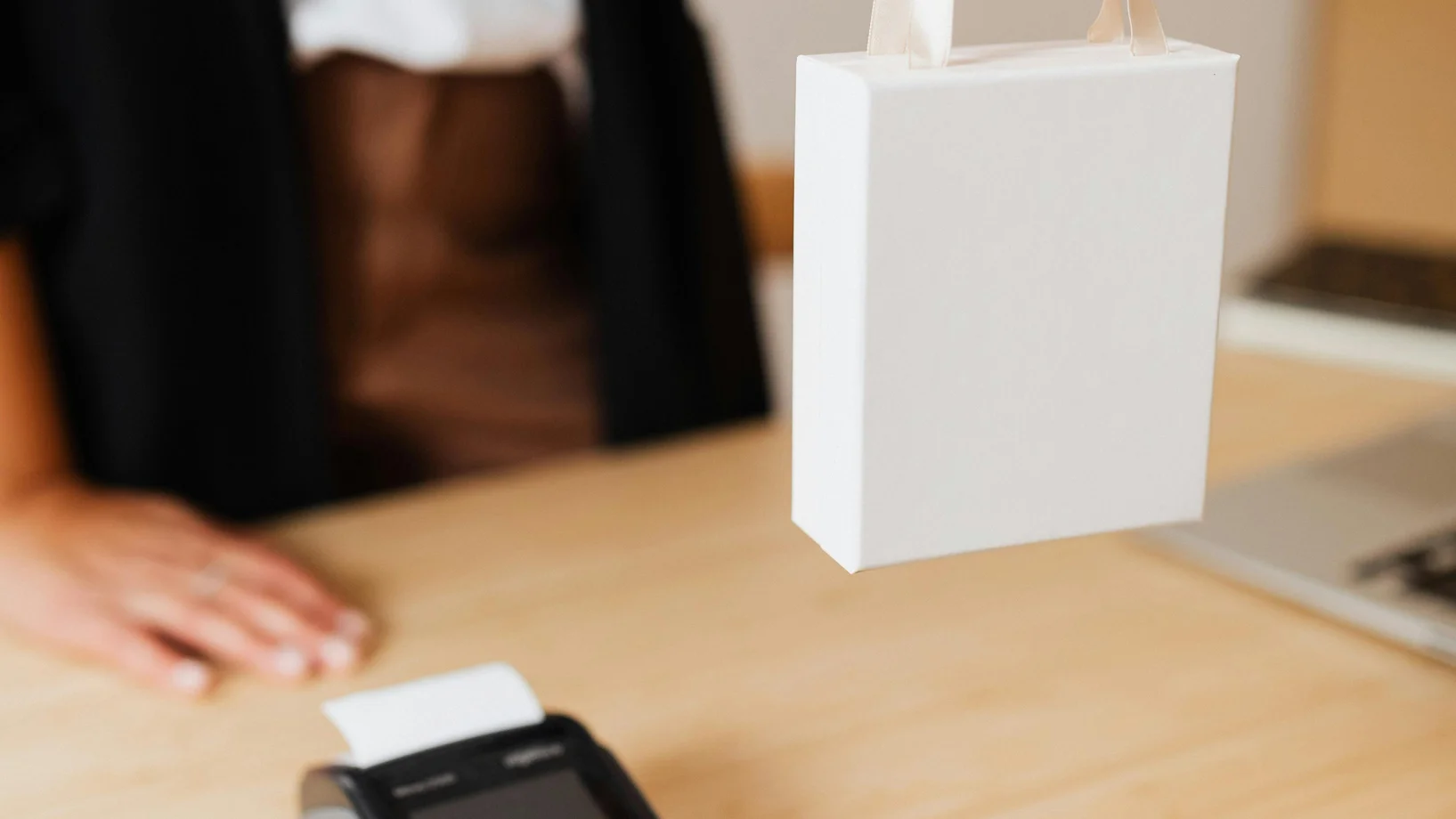 Close-up of shopper's hand holding a bag next to a payment terminal on a wooden counter.