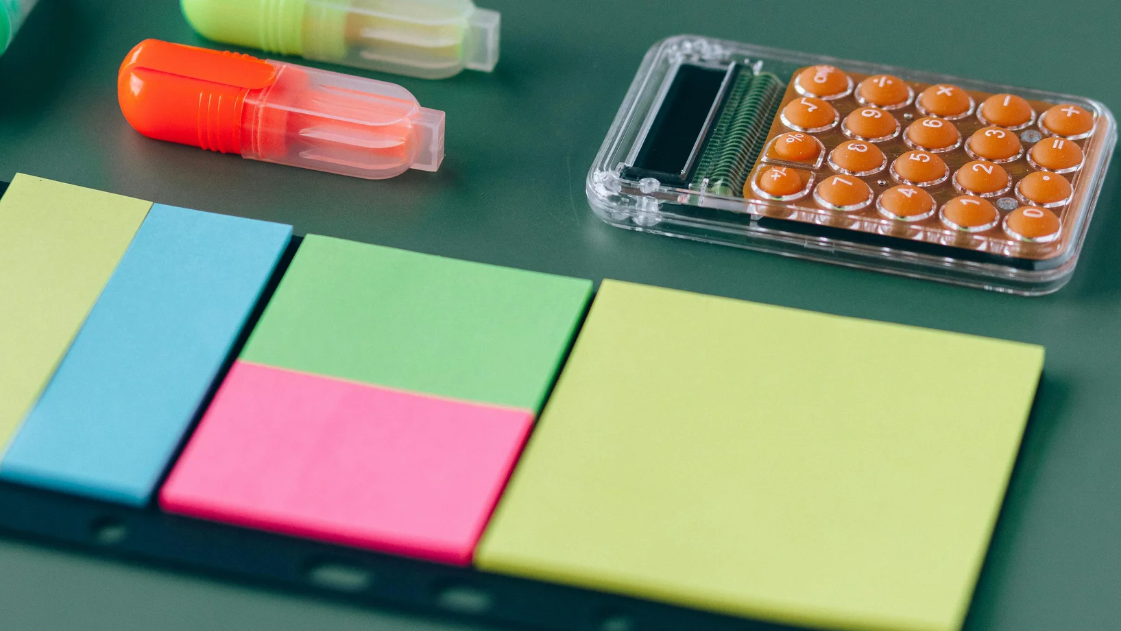 Assorted office supplies including sticky notes and highlighters on a green background.
