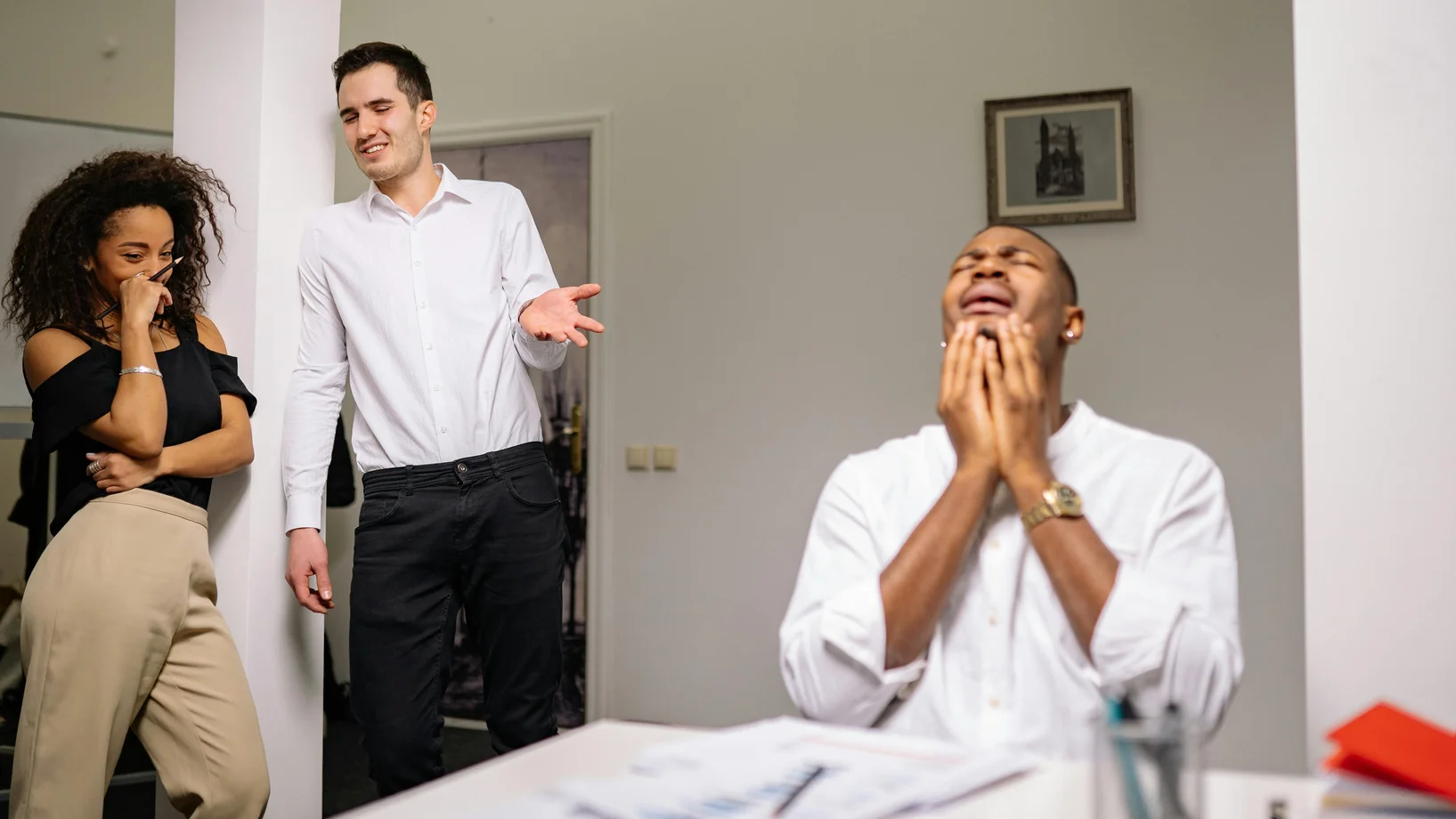 Three colleagues in an office setting display emotions of bullying and distress.