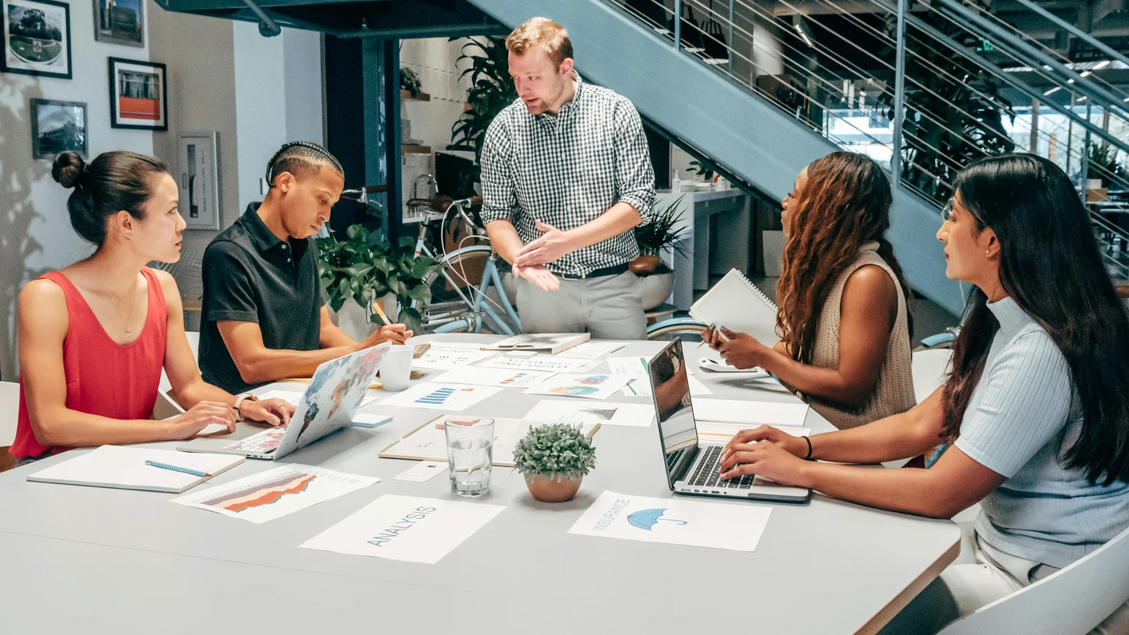 A diverse group of colleagues collaborating on a project in a modern office setting with laptops and documents.