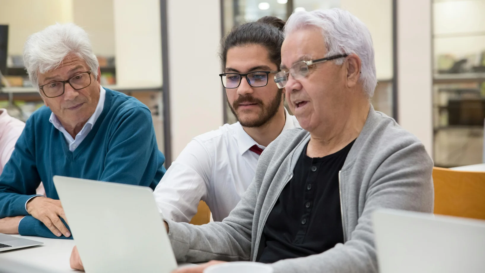 Three men collaborating and learning technology together on laptops indoors.