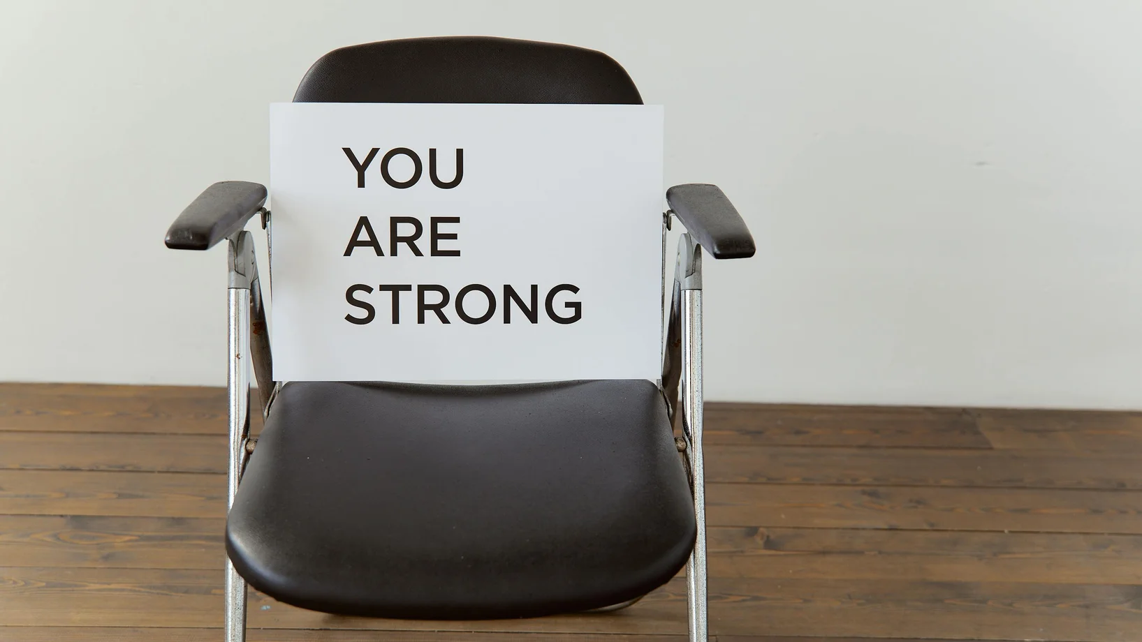 Black chair with 'You Are Strong' sign, symbolizing resilience.