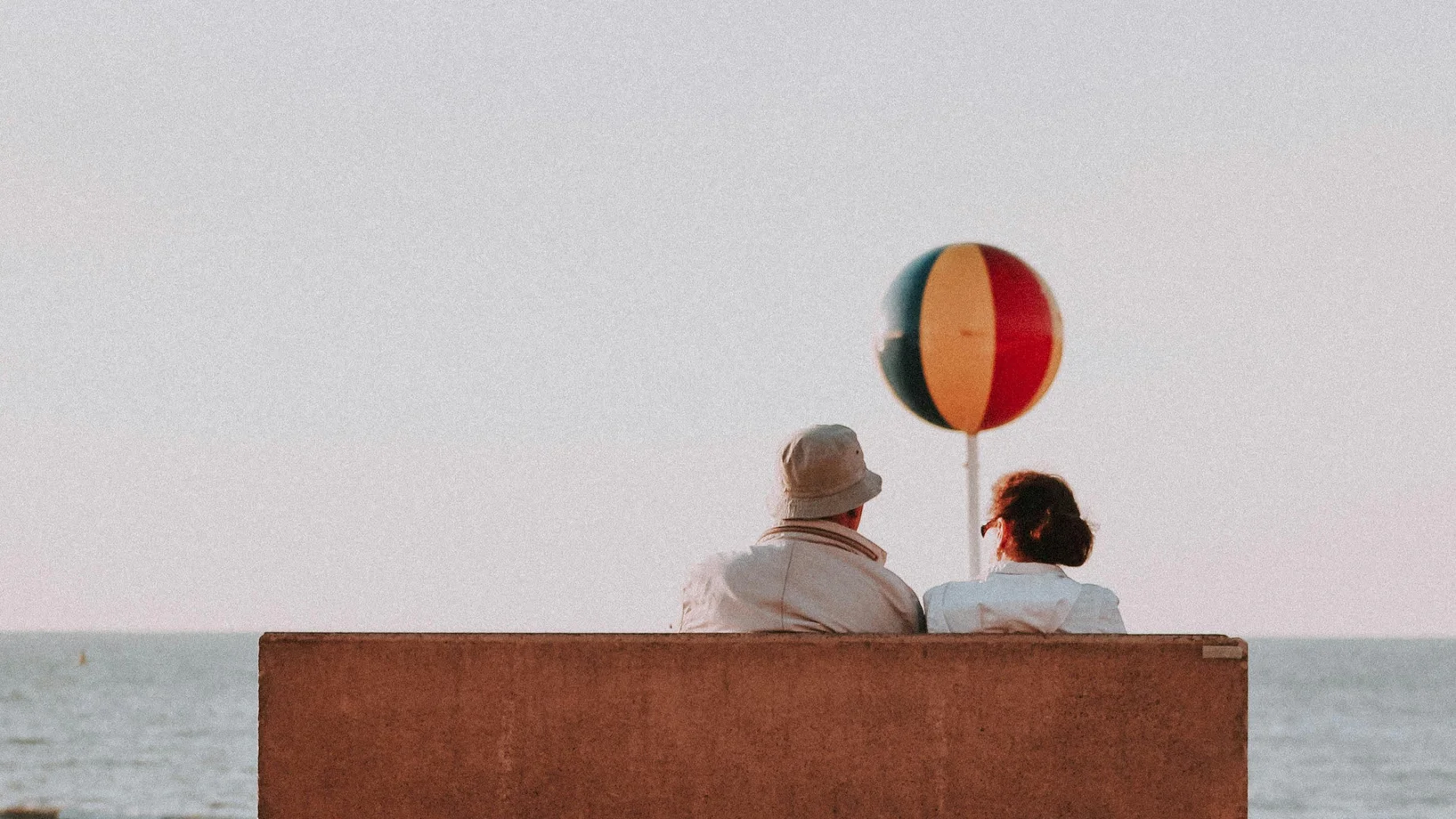 Back view of unrecognizable senior couple sitting on bench and admiring amazing seascape in summer