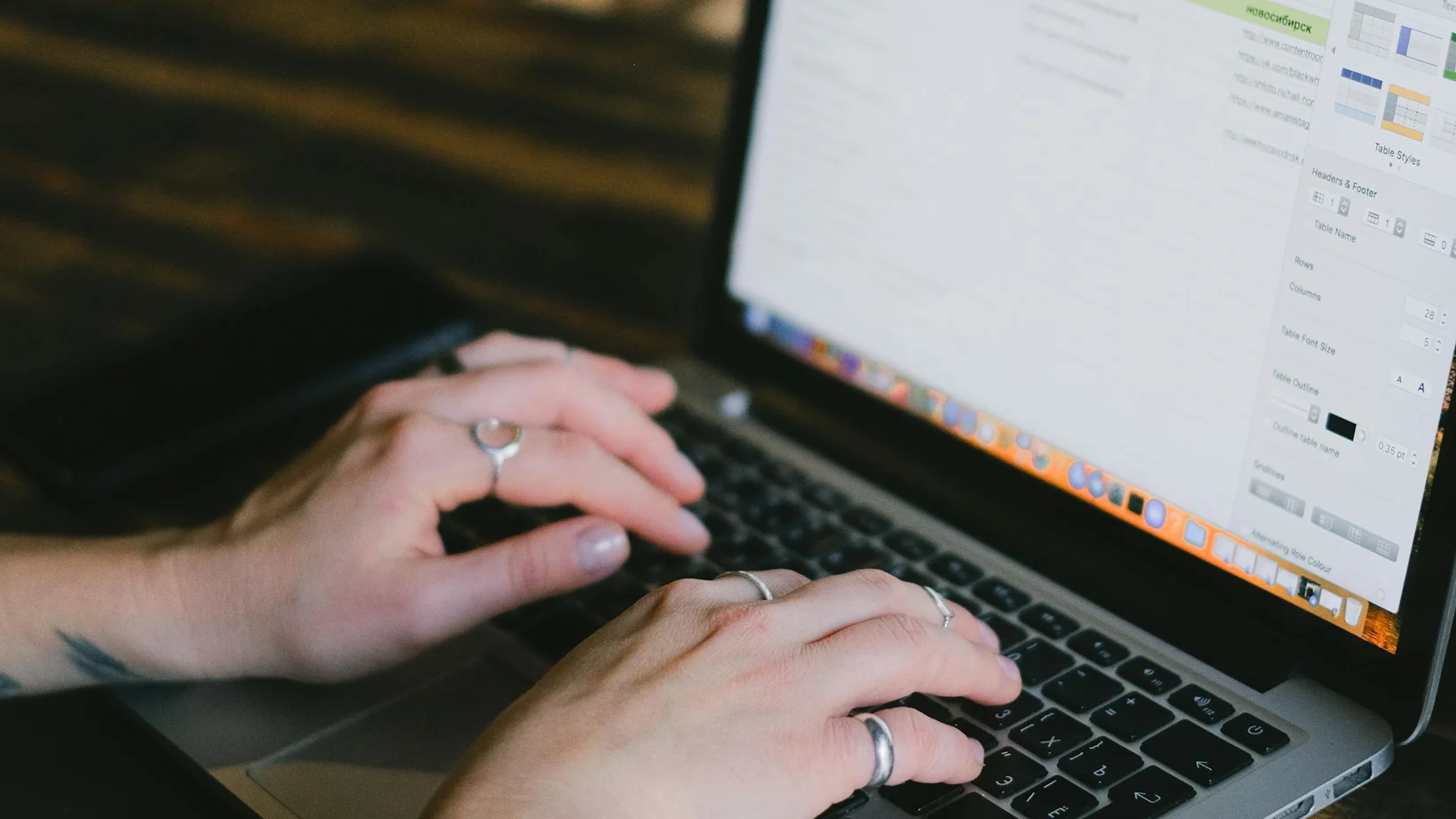 Unrecognizable busy female freelancer typing on keyboard of netbook while sitting at wooden counter during online work on remote project